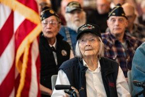 An audience of older veterans sits and listens 