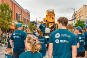 A group of Traverse City fiber employees are wearing branded t shirts walking in a city parade