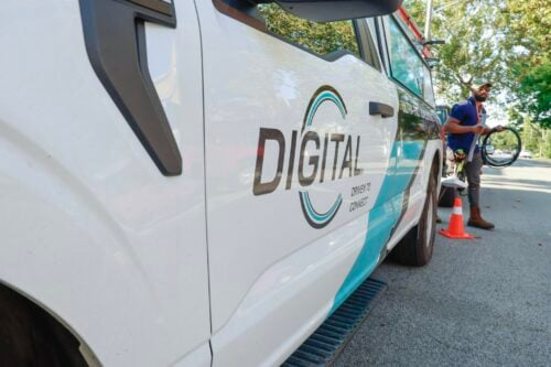 A DigitalC service van is parked on side of street with installer walking behind the van with a coiled cord in his hand