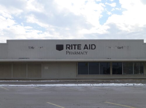 An abandoned commercial building still has visible remnants of a Rite Aid sign on its exterior. It's possible that a restrictive covenant has prevented another business from moving into this building.