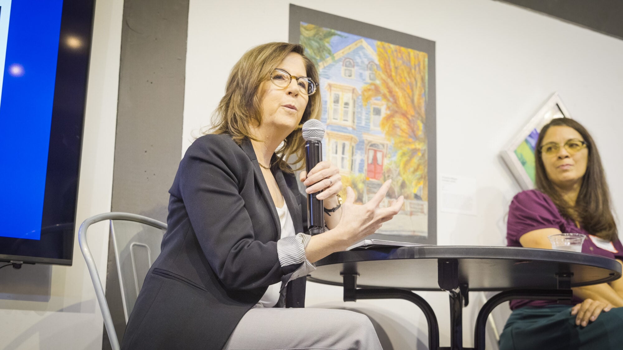 Local First AZ CEO Kimber Lanning speaks into a microphone while seated at a tall table.